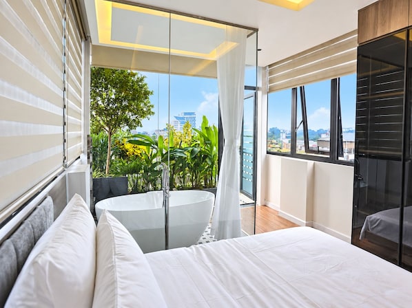 A modern bedroom with a large bed, a glass door leading to a balcony, and a view of the cityscape.