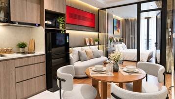A modern kitchen with a black refrigerator, a dining area with a round table and four chairs, a sofa, and a large window with curtains.