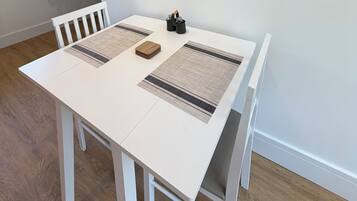A dining area with a white table, two woven placemats, and a painting of horses and sunflowers on the wall.