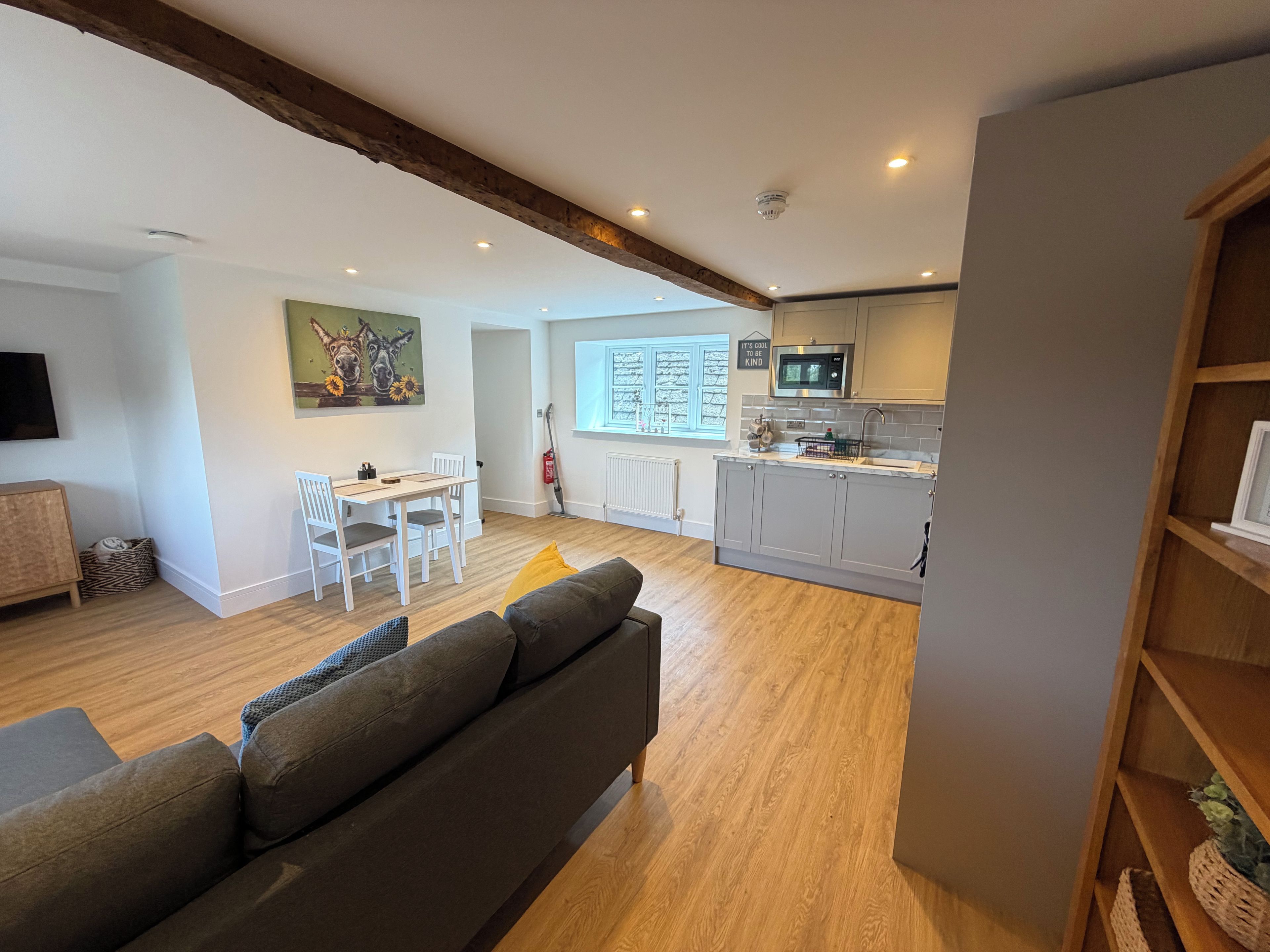 Una sala de estar moderna con un sofá gris, una mesa de comedor con sillas, y una zona de cocina con armarios grises y un microondas.