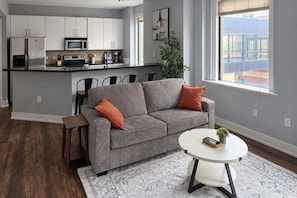 A modern living space with a grey sofa, a round coffee table, and a kitchen area with white cabinets and appliances.