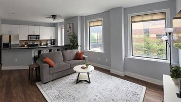 A modern living room with a grey sofa, a round coffee table, and a kitchen in the background.