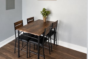 A dining table with four chairs, a potted plant, and a light switch on the wall.