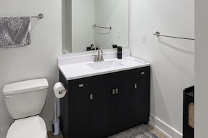 A modern bathroom with a white sink, black cabinets, a toilet, and a mirror.