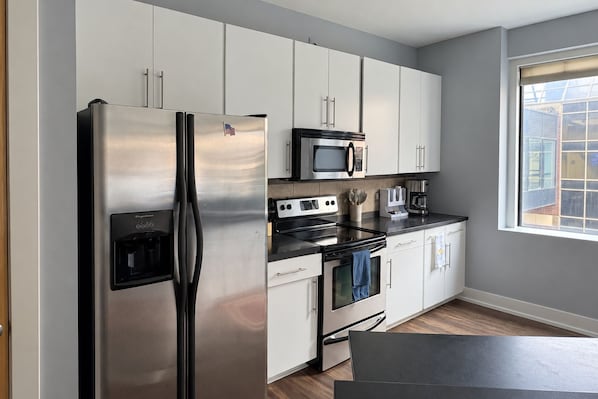 A modern kitchen with stainless steel appliances, white cabinetry, and a window providing natural light.