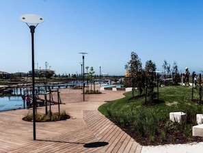 Un muelle de madera con un farol, un área verde y una masa de agua.