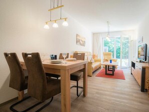 Ein Essbereich mit einem Holztisch und Stühlen, einer Couch, einem Fernseher und einer Glastür zum Balkon.