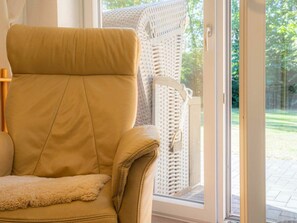 A tan leather chair with a fluffy cushion, positioned near a white wicker chair and a glass door leading outside. - 6 in the House Bovergeest 3 (St. Peter-Ording)