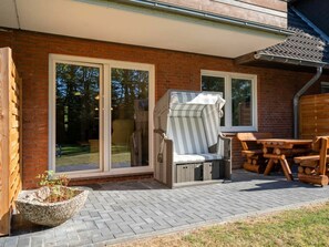 Eine Terrasse mit einem Holztisch und -stühlen, einem Korbstuhl und einem Steinpflanzgefäß.