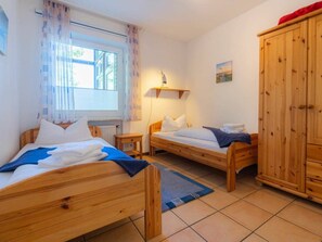 A room with two wooden beds, a window with curtains, a wooden wardrobe, and a small shelf with a lamp. - 6 in the House Bovergeest 3 (St. Peter-Ording)