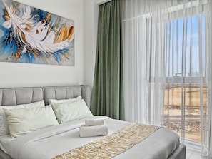 A hotel room with a large bed, a painting on the wall, and a view of a desert landscape through the window. - Stylish 2BR | Creek Beach | Dubai Creek Harbour (Dubai)