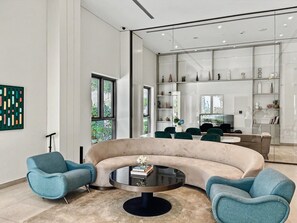 Ein modernes Wohnzimmer mit einer gebogenen Couch, zwei Sesseln, einem Couchtisch und einer Glastrennwand mit Regalen.