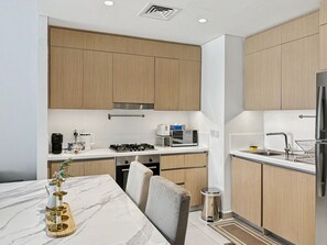 A modern kitchen with wooden cabinets, a marble countertop, and stainless steel appliances. - Stylish 2BR | Creek Beach | Dubai Creek Harbour (Dubai)