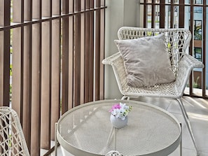 A wicker chair with a cushion, a round metal table with a vase of flowers, and a view of a building through a metal fence. - Stylish 2BR | Creek Beach | Dubai Creek Harbour (Dubai)