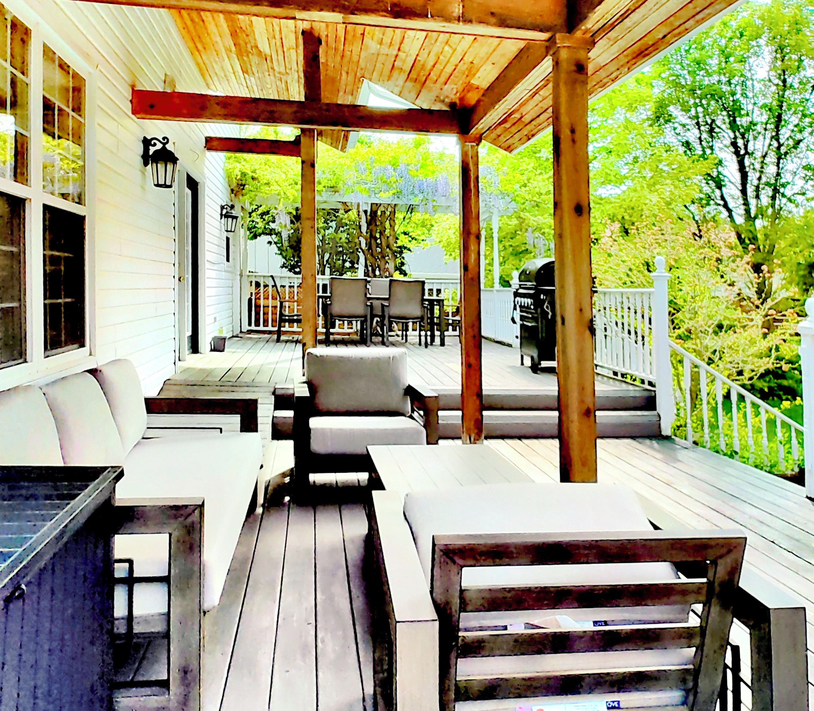 A covered outdoor deck with wooden furniture and a grill.