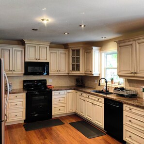 A kitchen with white cabinets, a black stove, and a black dishwasher. - L&V | Victorian Garden Retreat | 3BR| Spacious Deck | Walk to Historic Old Town (Niagara-on-the-Lake)