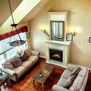 A living room with a fireplace, two sofas, a coffee table, and a hanging light fixture. - L&V | Victorian Garden Retreat | 3BR| Spacious Deck | Walk to Historic Old Town (Niagara-on-the-Lake)