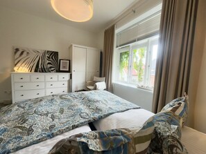 Une chambre à coucher avec un lit, une commode, une fenêtre avec des rideaux et un luminaire au plafond.