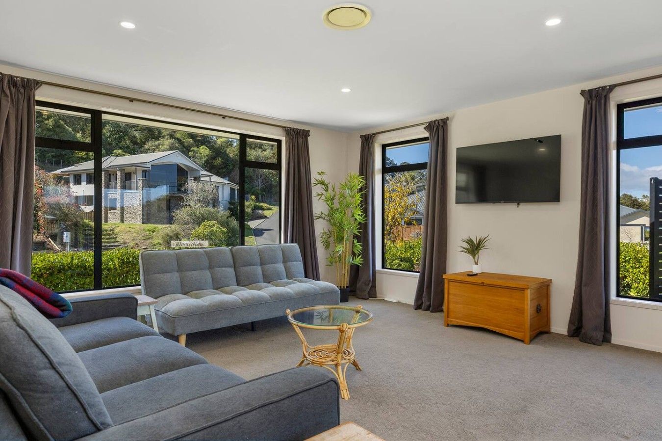 A modern living room with a grey sofa, a glass coffee table, and a TV on the wall.