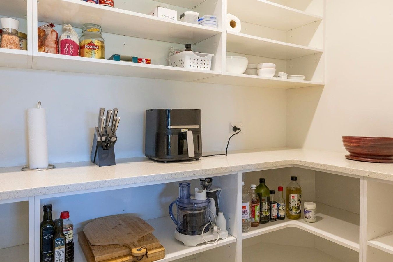 A kitchen with white shelves, a coffee maker, a blender, and various kitchen items.