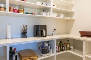 Une cuisine avec des étagères blanches, une machine à café, un mixeur et divers ustensiles de cuisine.