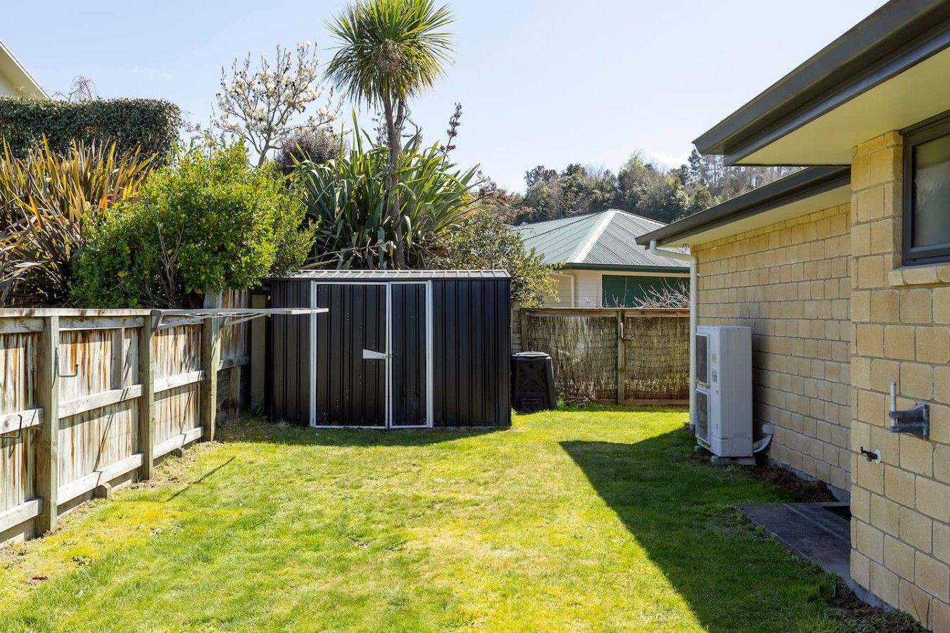 A backyard with a fenced area, a shed, and a house with a brick exterior.