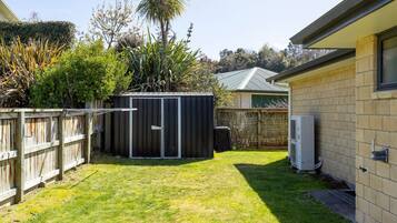 A backyard with a fenced area, a shed, and a house with a brick exterior.