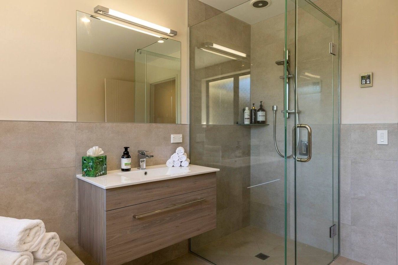 A modern bathroom with a glass shower enclosure, a vanity with a mirror, and toiletries.