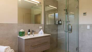 A modern bathroom with a glass shower enclosure, a vanity with a mirror, and toiletries.