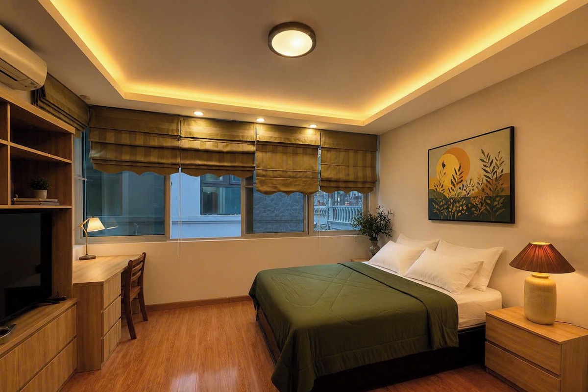 Un dormitorio con cama, mesita de noche, lámpara, ventana con cortinas y un cuadro en la pared.