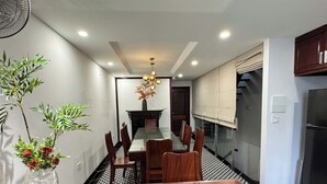 A modern kitchen with a dining area, featuring a wooden table, chairs, a vase with flowers, and a hanging light fixture. - Joy Classic Apartment - PKB (Ba Đình)