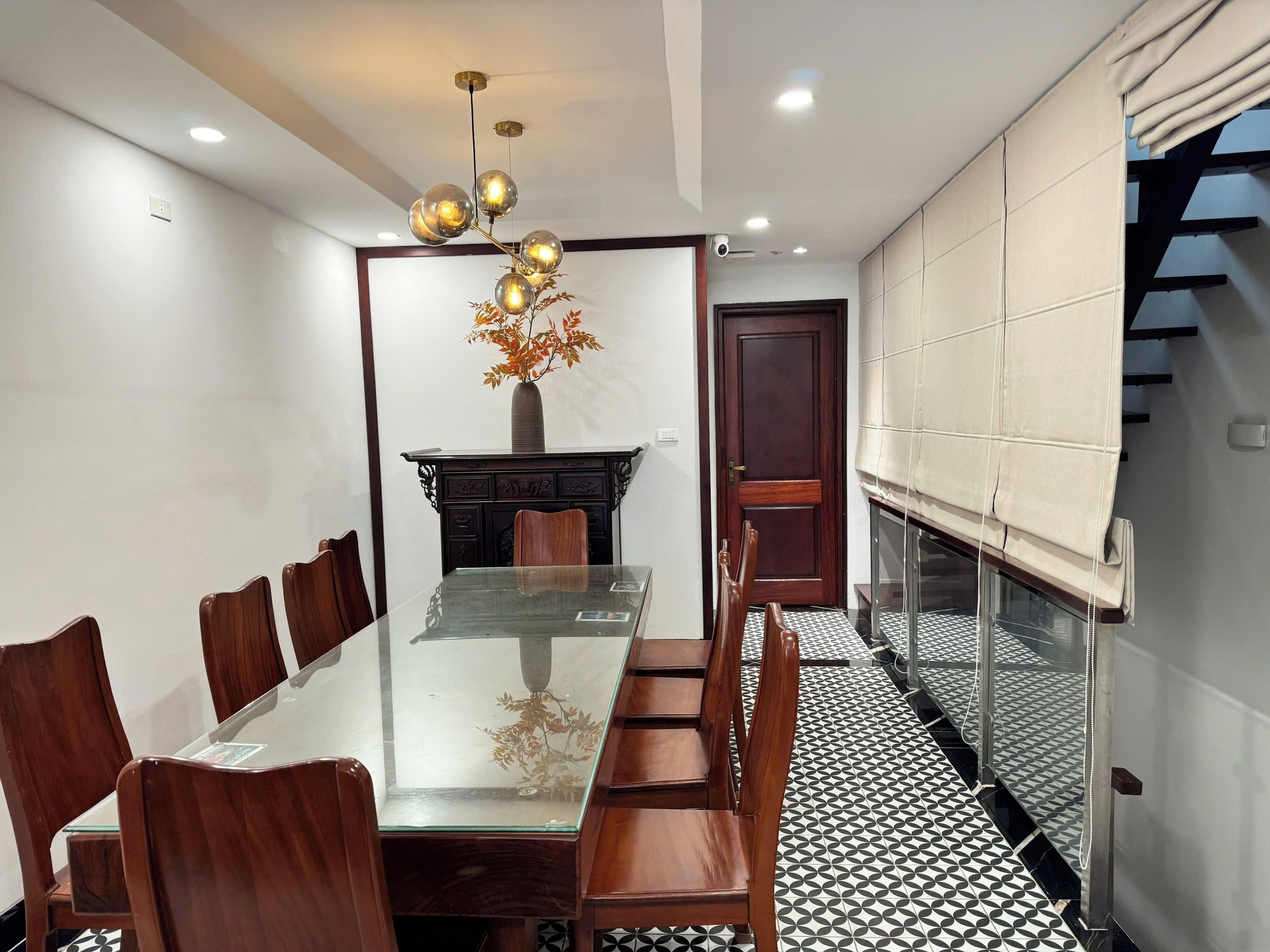 Un comedor con una mesa de vidrio, sillas de madera, un jarrón decorativo y un piso con diseño.