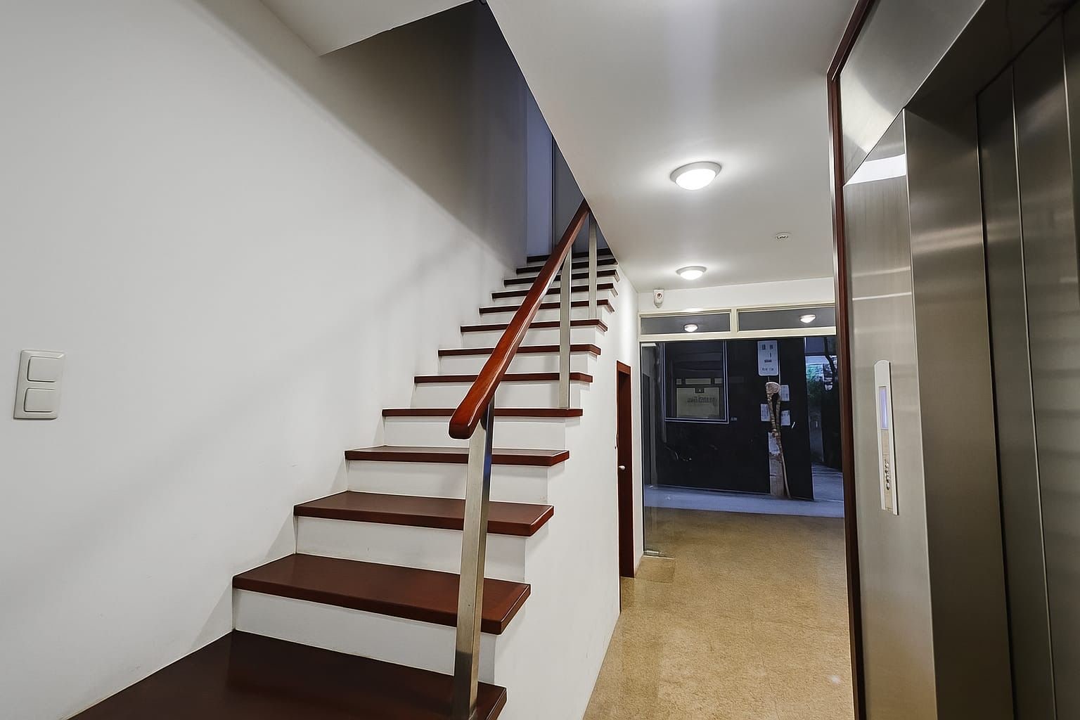 A modern interior with a wooden staircase, a hallway, and an elevator.