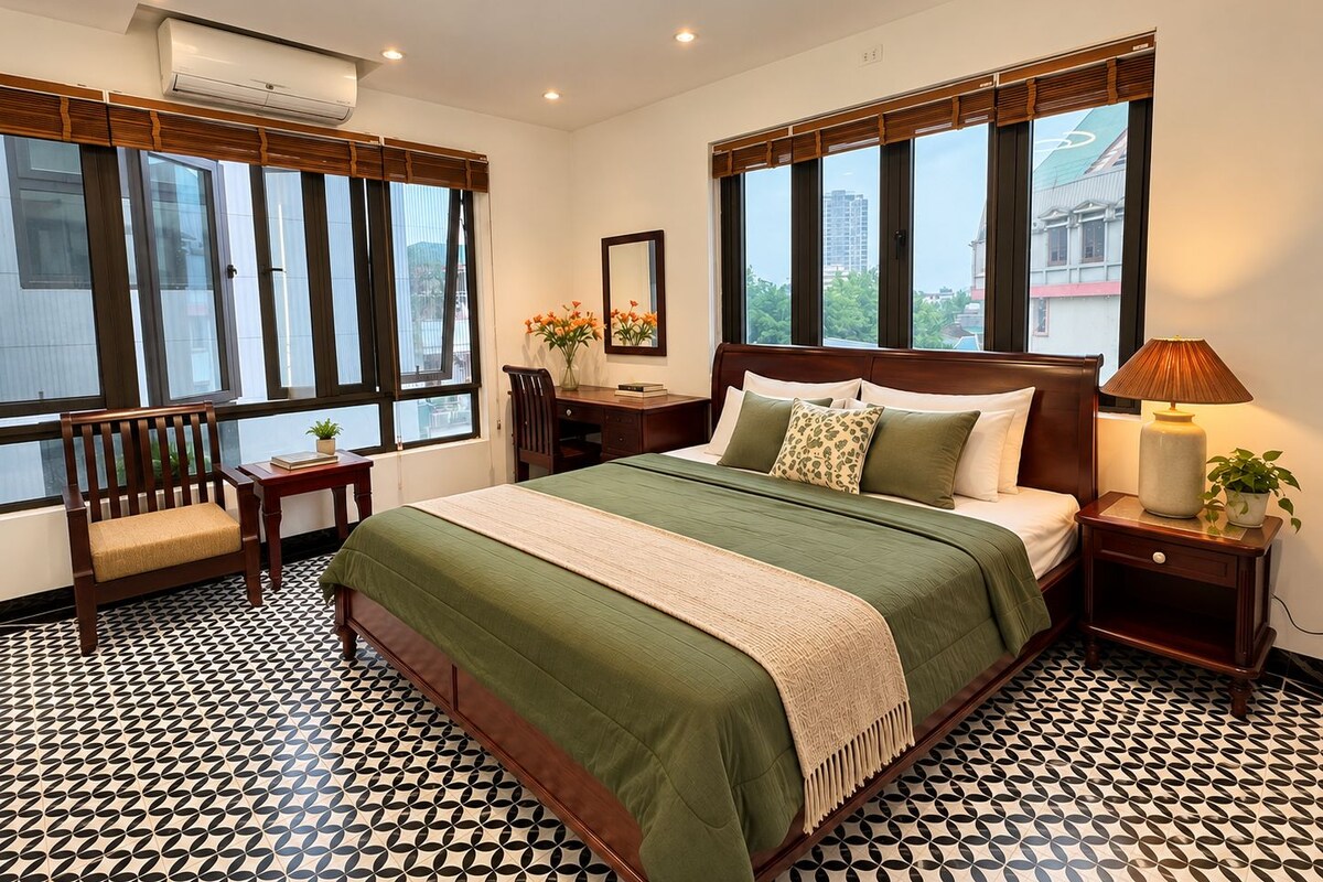 A hotel room with a large bed, a desk, a chair, and a window with a city view.