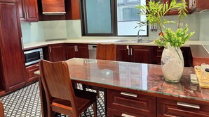 A kitchen with wooden cabinets, a glass-top table, and a potted plant. - Joy Classic Apartment - PKB (Ba Đình)