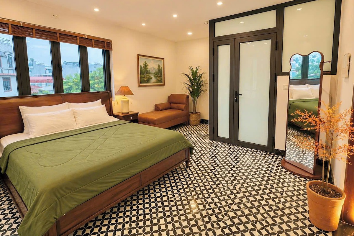 Un dormitorio con una cama, una silla, una lámpara, un cuadro y una planta en maceta.