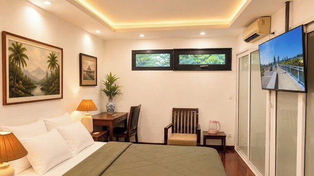 A hotel room with a bed, bedside lamps, a chair, a small table, and a TV. - Joy Classic Apartment - PKB (Ba Đình)