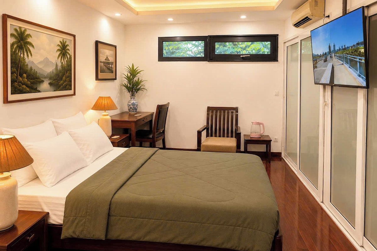 Una habitación de hotel con una cama, lámparas de noche, una silla, una mesita y un televisor.