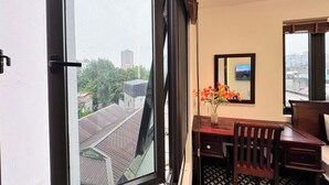 A room with a large window, a wooden desk, a chair, a vase with flowers, and a framed picture on the wall. - Joy Classic Apartment - PKB (Ba Đình)