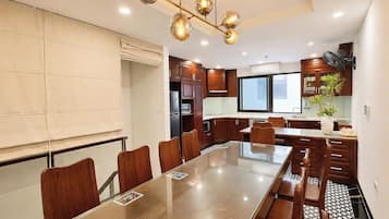 Uma cozinha moderna com uma mesa de jantar comprida, cadeiras de madeira e uma luminária pendente.