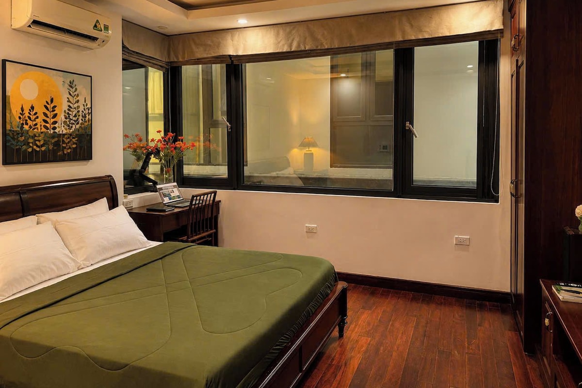 Habitación de hotel con cama, escritorio, silla, ventanal con vidrio esmerilado y unidad de aire acondicionado.