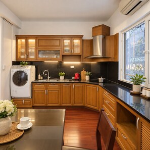 A modern kitchen with wooden cabinets, a built-in washing machine, and a window with a view. - Joy Classic Apartment - PKB (Ba Đình)