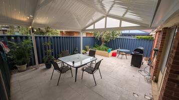 A covered patio area with a table and chairs, a barbecue grill, and potted plants.