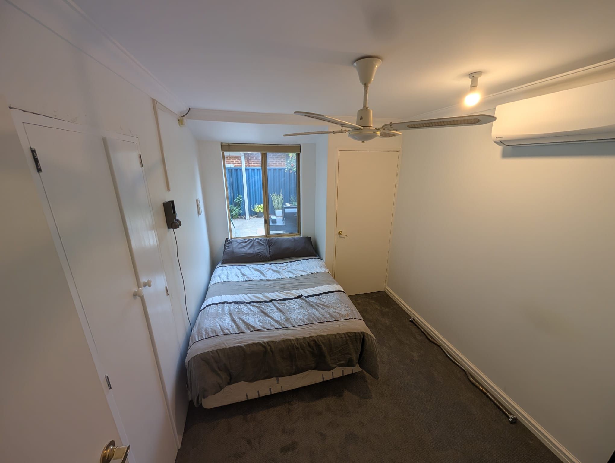 A bedroom with a bed, a ceiling fan, a window, and a door.