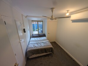 Quarto com cama, ventilador de teto, janela e porta.