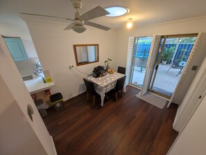 Espaço de refeições com mesa, cadeiras, ventilador de teto e vista do quintal por uma porta de correr de vidro.
