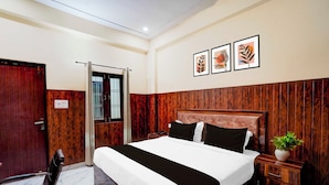 A hotel room with a wooden headboard, a bed with white and black bedding, a desk with a chair, and a potted plant. - Super Townhouse Matiyari (Lucknow)