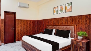 A bedroom with a wooden headboard, a bed with black and white bedding, a bedside table with a plant, and a marble floor. - Super Townhouse Matiyari (Lucknow)