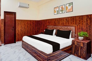 A bedroom with a wooden headboard, a bed with black and white bedding, a bedside table with a plant, and a marble floor. - Super Townhouse Matiyari (Lucknow)