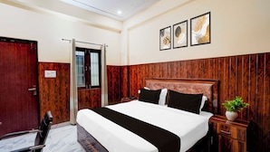 A hotel room with a wooden headboard, a bed with black and white bedding, a bedside table with a plant, and a window with bars. - Super Townhouse Matiyari (Lucknow)